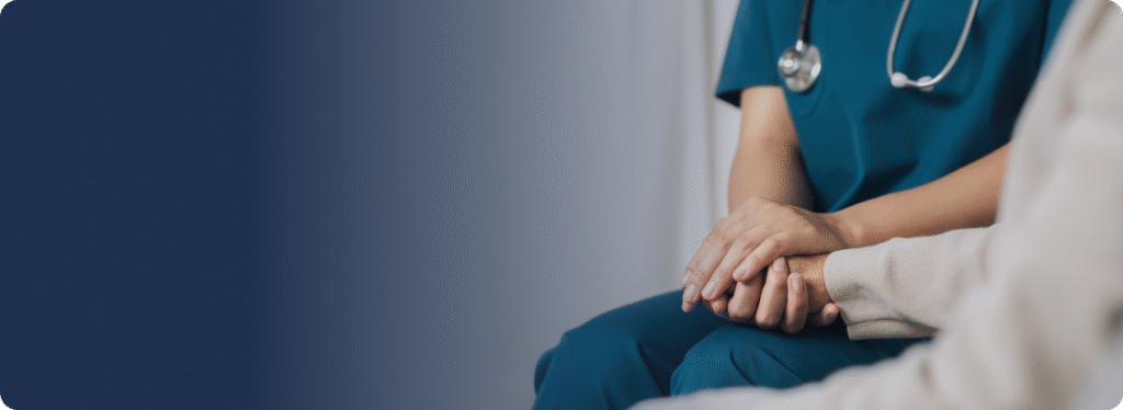 Older adult sitting with a caregiver providing comfort at home.