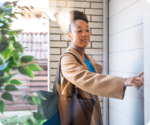Woman opening her front door and greeting a visitor with a warm smile.