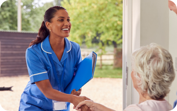 Nurse in blue scrubs talking with an older adult at home.