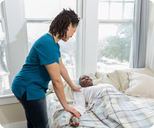 Caregiver helping an older adult adjust comfortably while resting in bed.