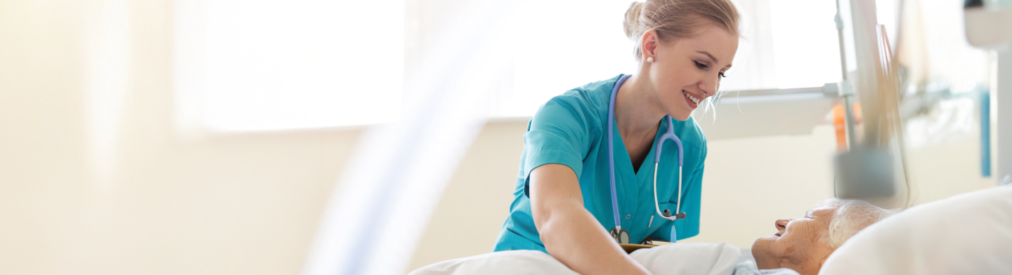 Clinician in blue scrubs smiling while reviewing paperwork in a bright care setting.