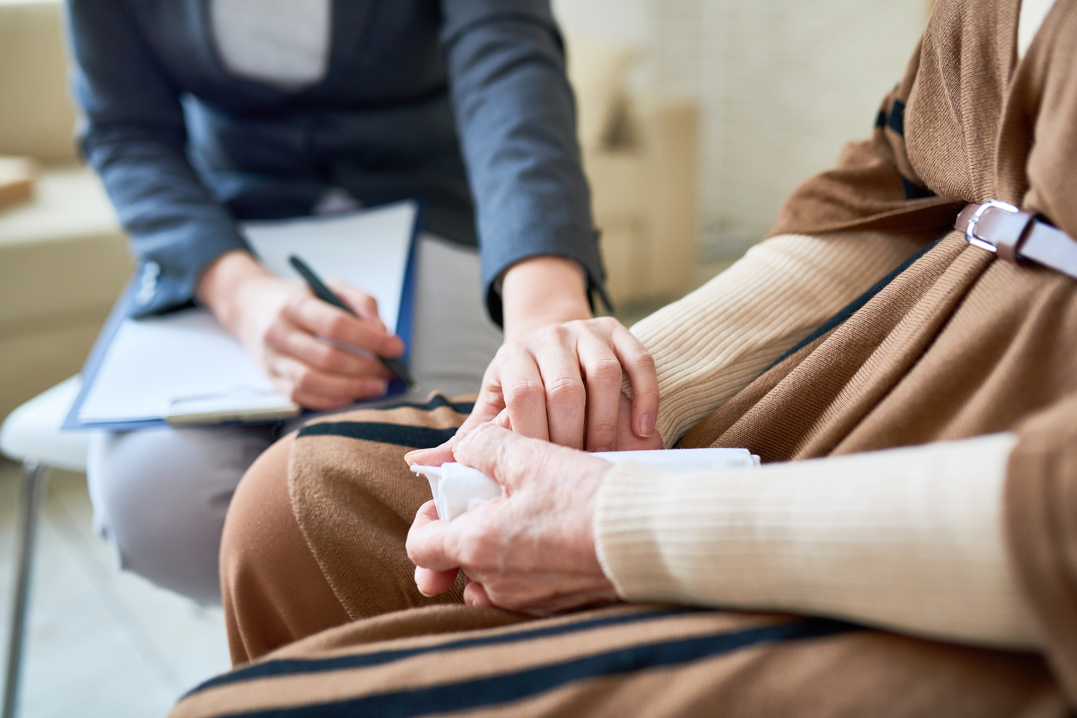 Caregiver sitting with an individual, offering support while taking notes during a counseling session