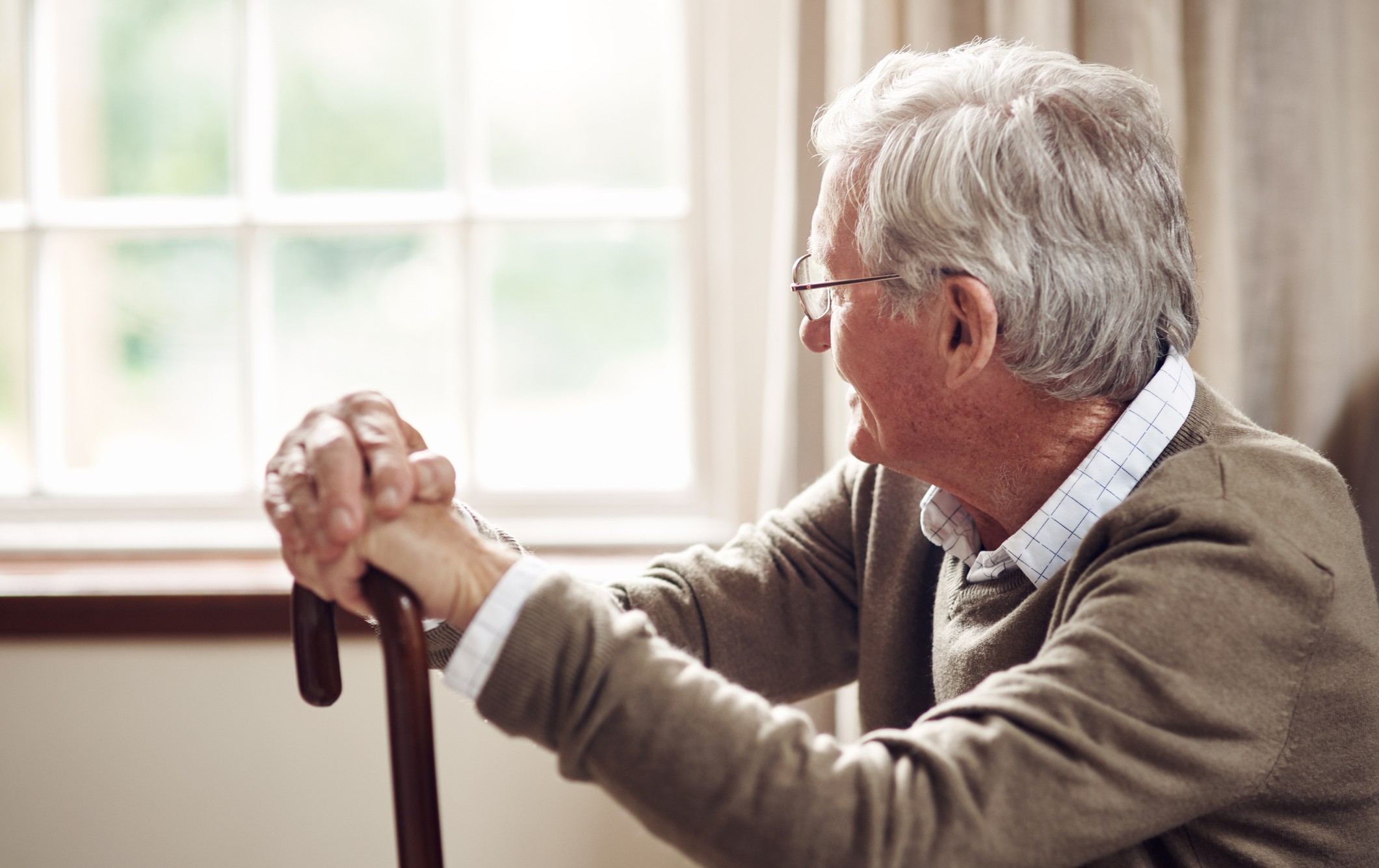 Senior man sitting by a window in reflection, representing thoughtful advance care planning decisions